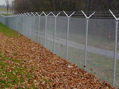 Zinc coated chain link anti-intruder fence with double extension arms and barbed wire topping for forest protection.