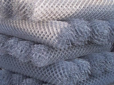 Several rolls of galvanized chain link fences are piled up.