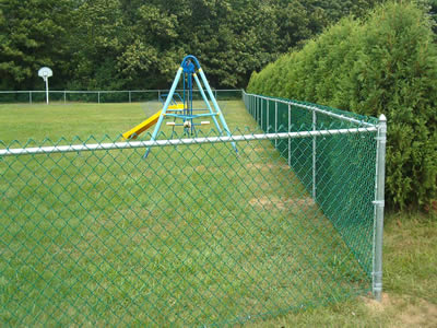 A green PVC coated wire chain link football fence is short and installed on a piece of grassland.