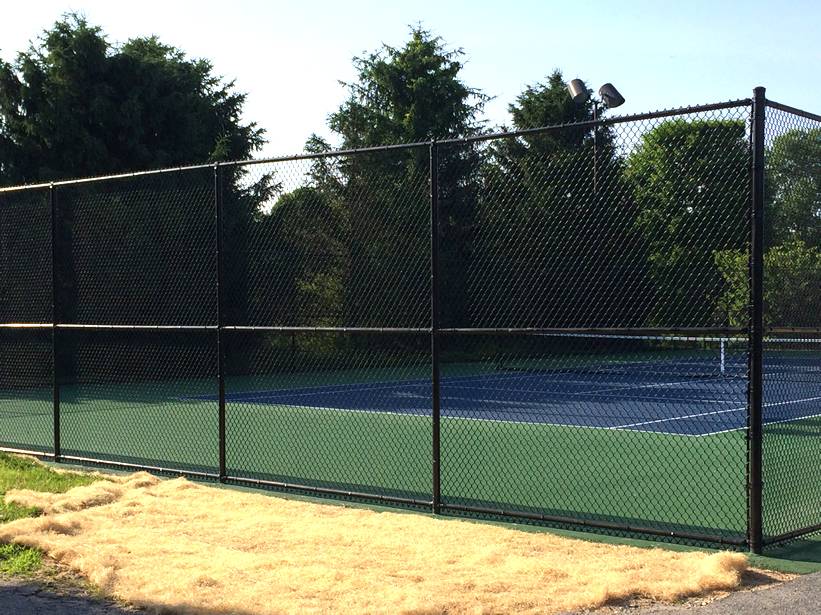 Black polymer-coated chain link tennis courts fencing with continuous middle rails.