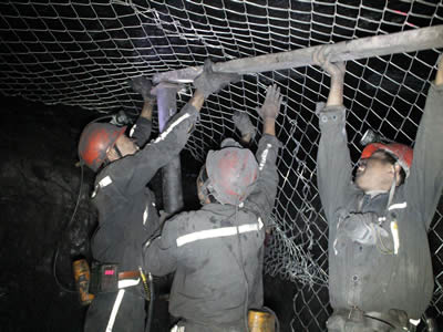 Workers are installing the underground chain link support mesh in soft rock mining roadway.