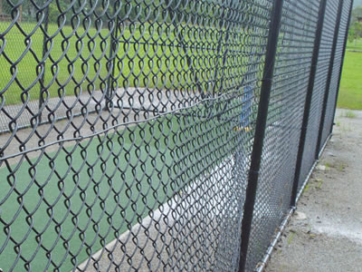 This is black cricket enclosure with four a cable wire tied onto the post and fabric chain link diamond.