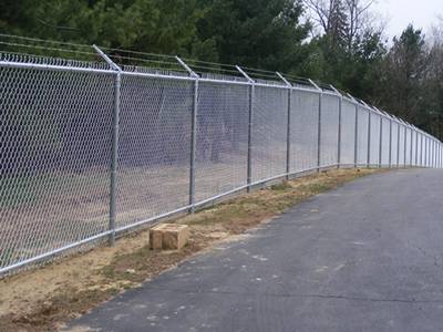Zinc coated chain link anti-intruder fence with single extension arms and barbed wire topping for road protection.