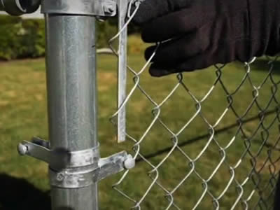 A working wearing gloves are installing the tension bar on the chain link fence.